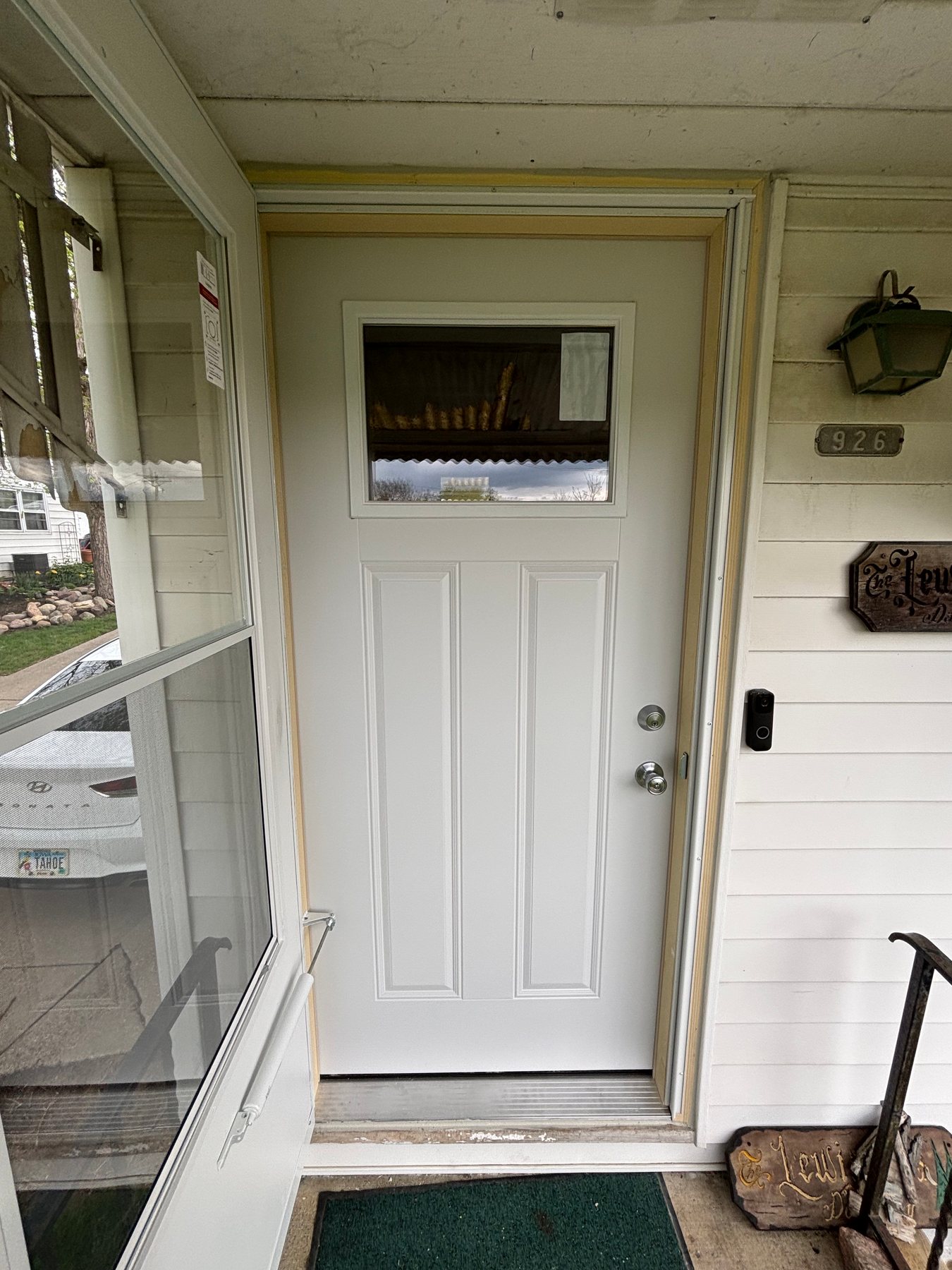 A newly installed white front entry door with a top window insert, silver hardware, and unfinished light wood trim on a house with light horizontal siding.