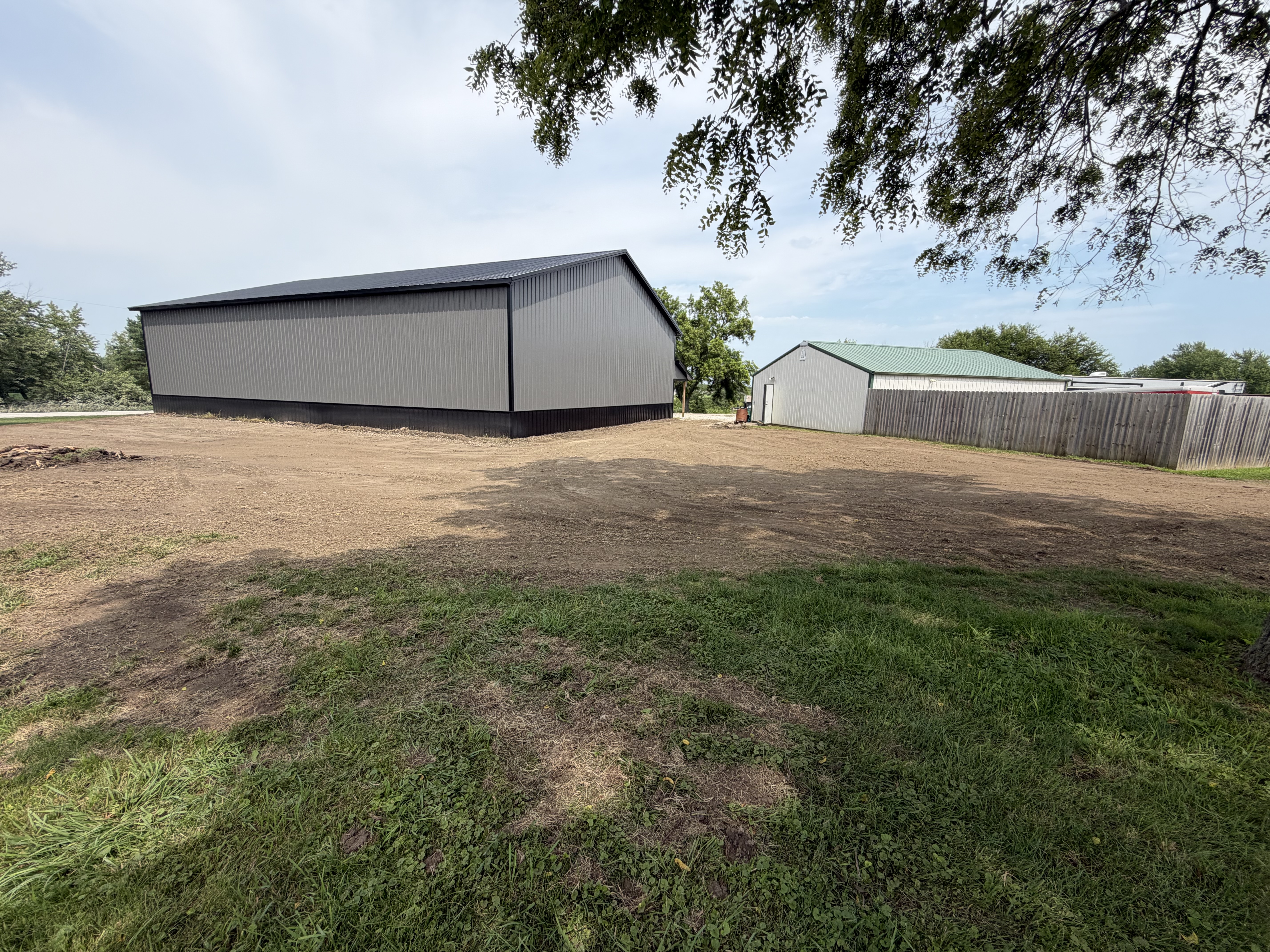 A newly graded dirt yard area surrounds a large grey metal outbuilding with black trim.