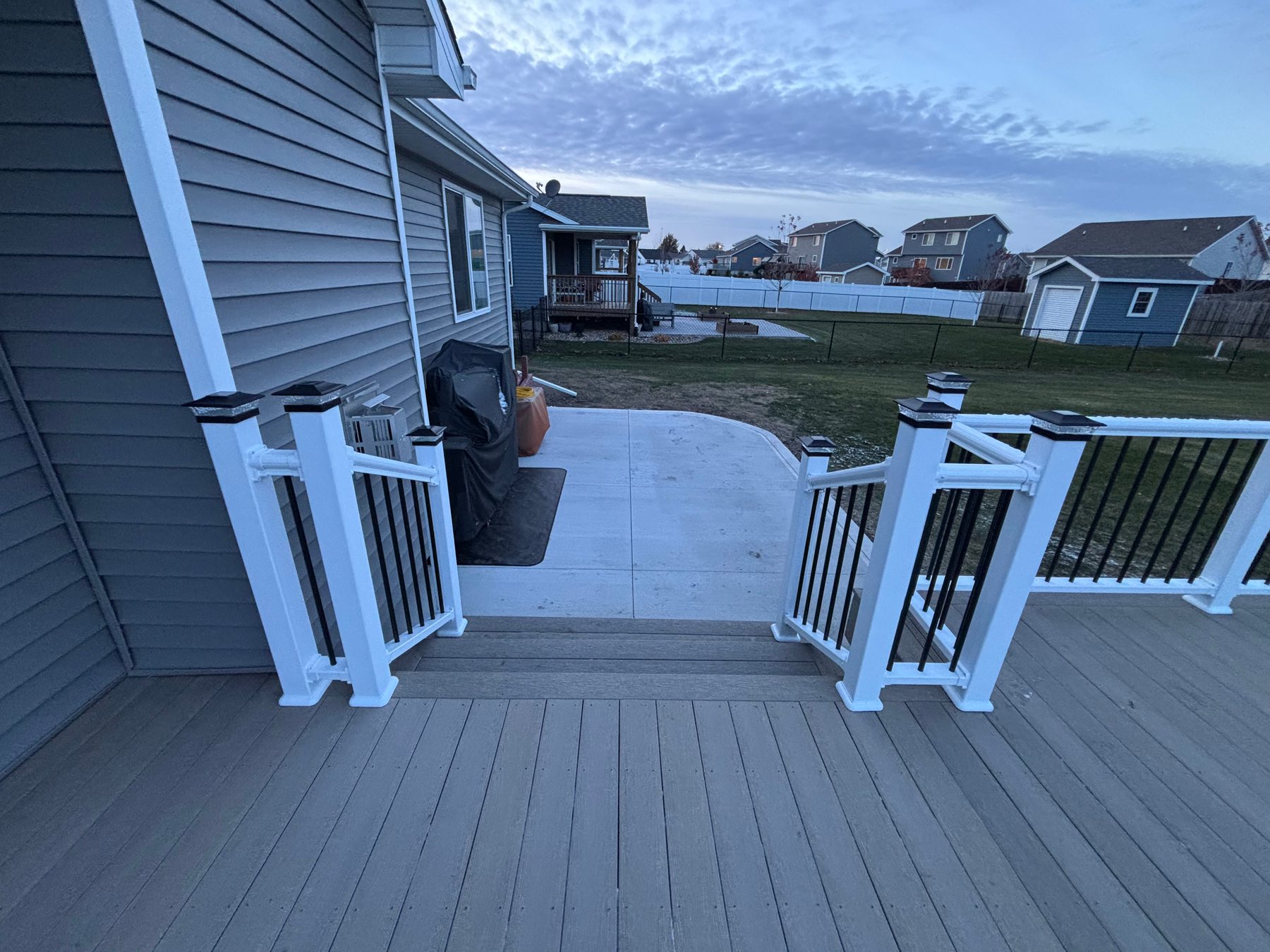 Grey composite deck with white railings and black balusters, with stairs leading down to a concrete patio.