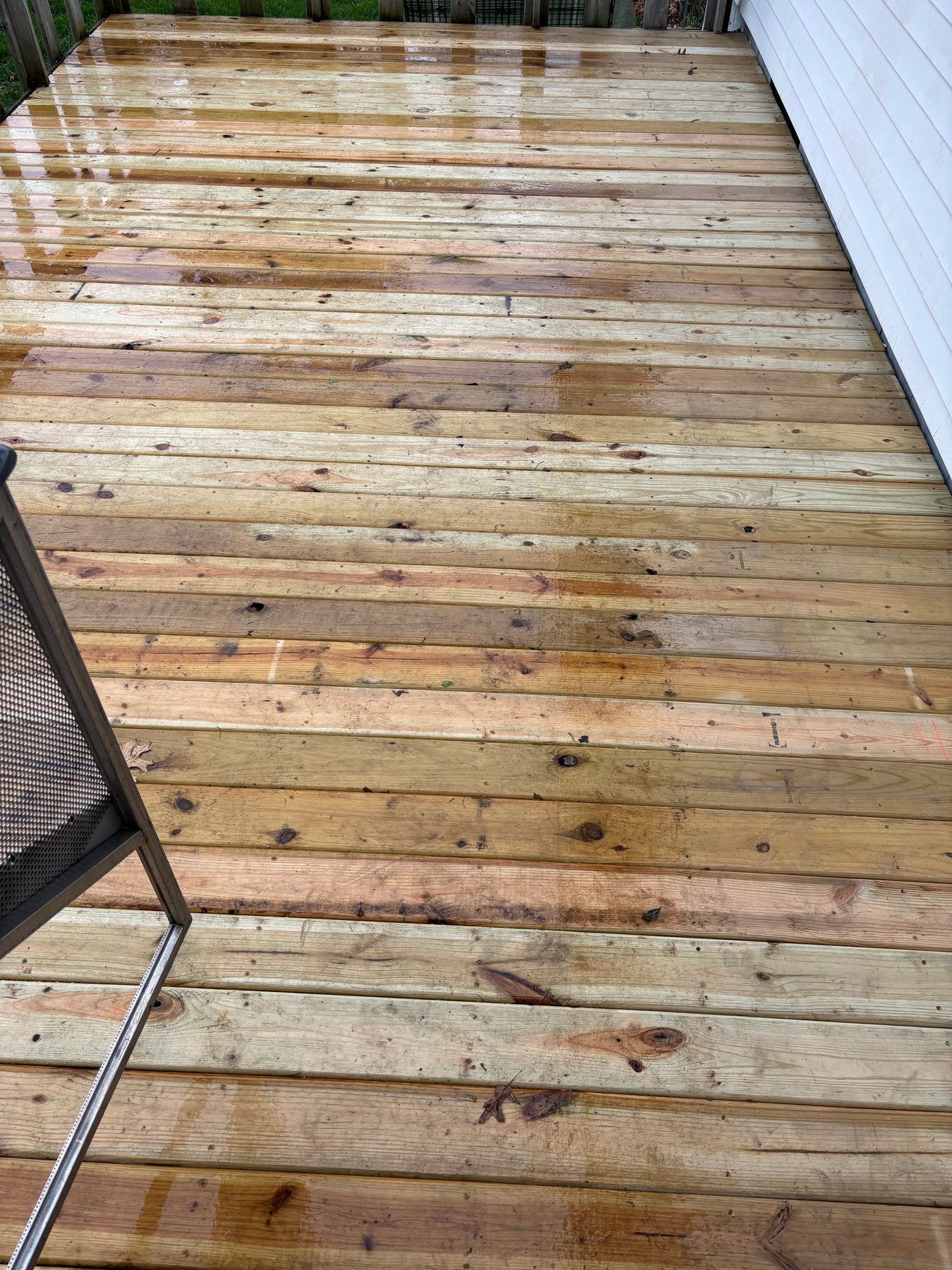 Freshly installed pressure-treated wood deck boards with a wet finish, showing natural wood grain and knots next to white vinyl siding.