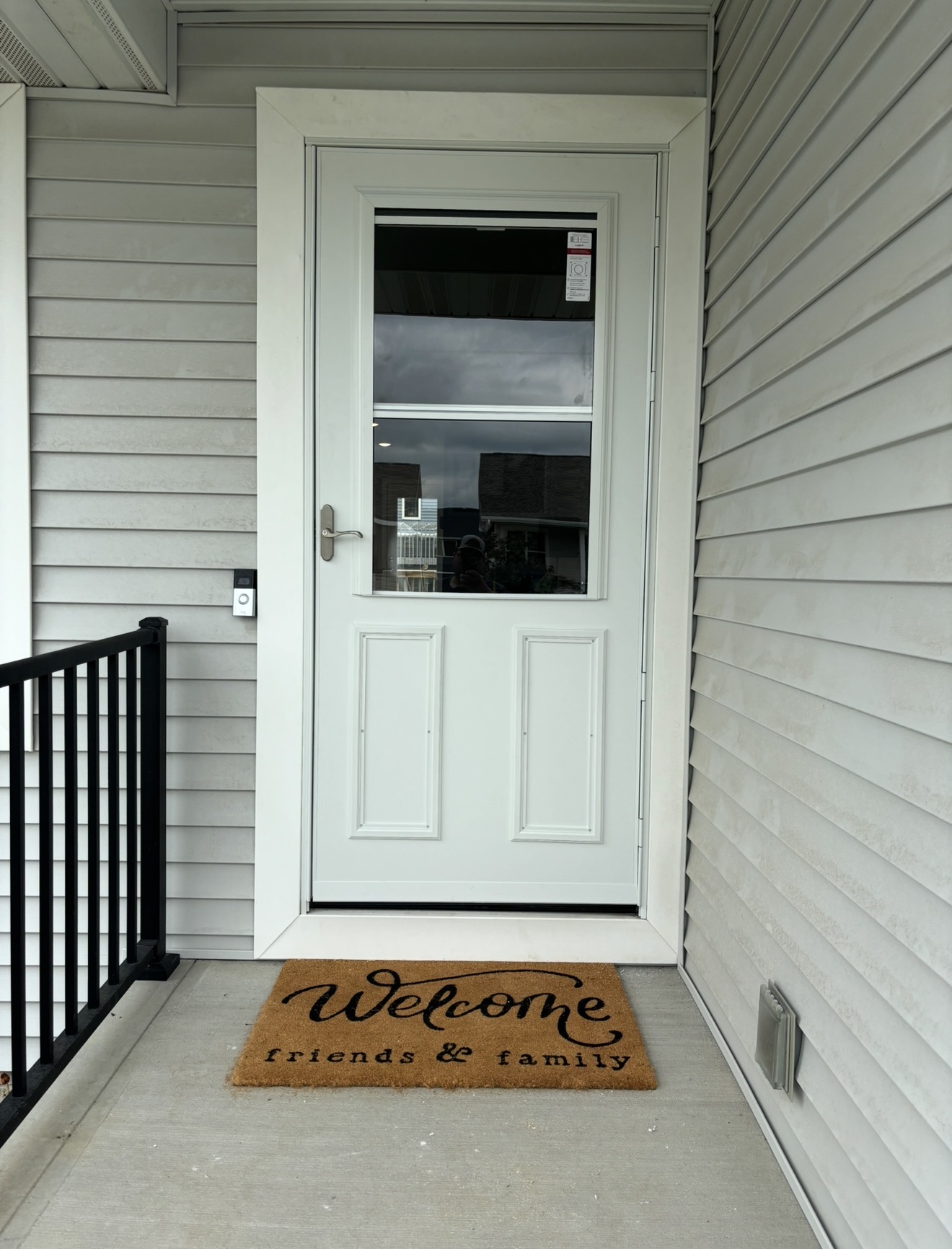A white exterior door with a glass window and white trim, installed on a concrete porch with light gray vinyl siding.