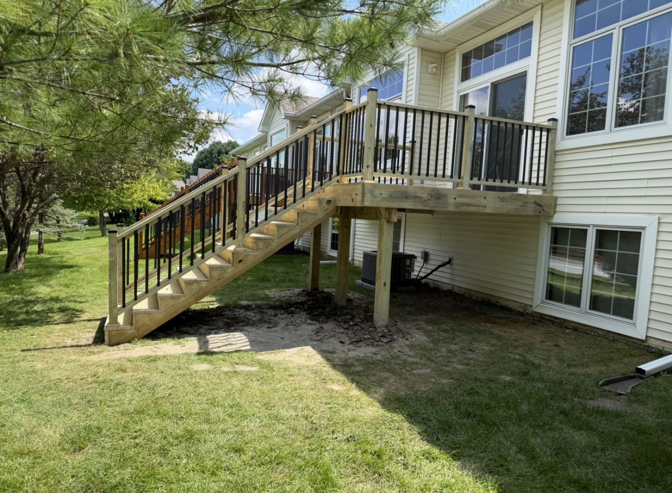 An elevated pressure-treated wood deck with black metal balusters and stairs attached to a home with beige siding.