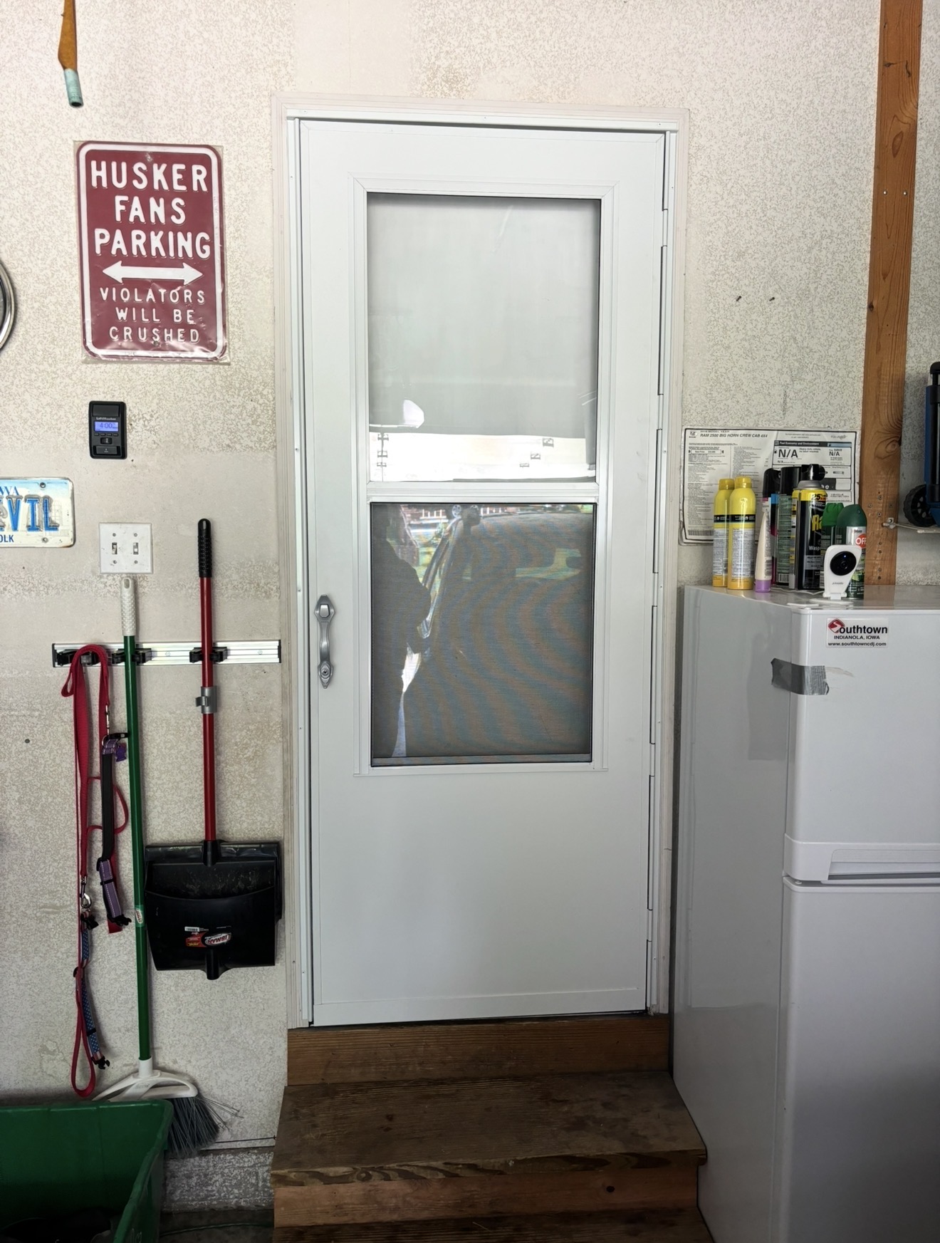 A white storm door with glass and screen panels installed above wooden steps inside a garage.