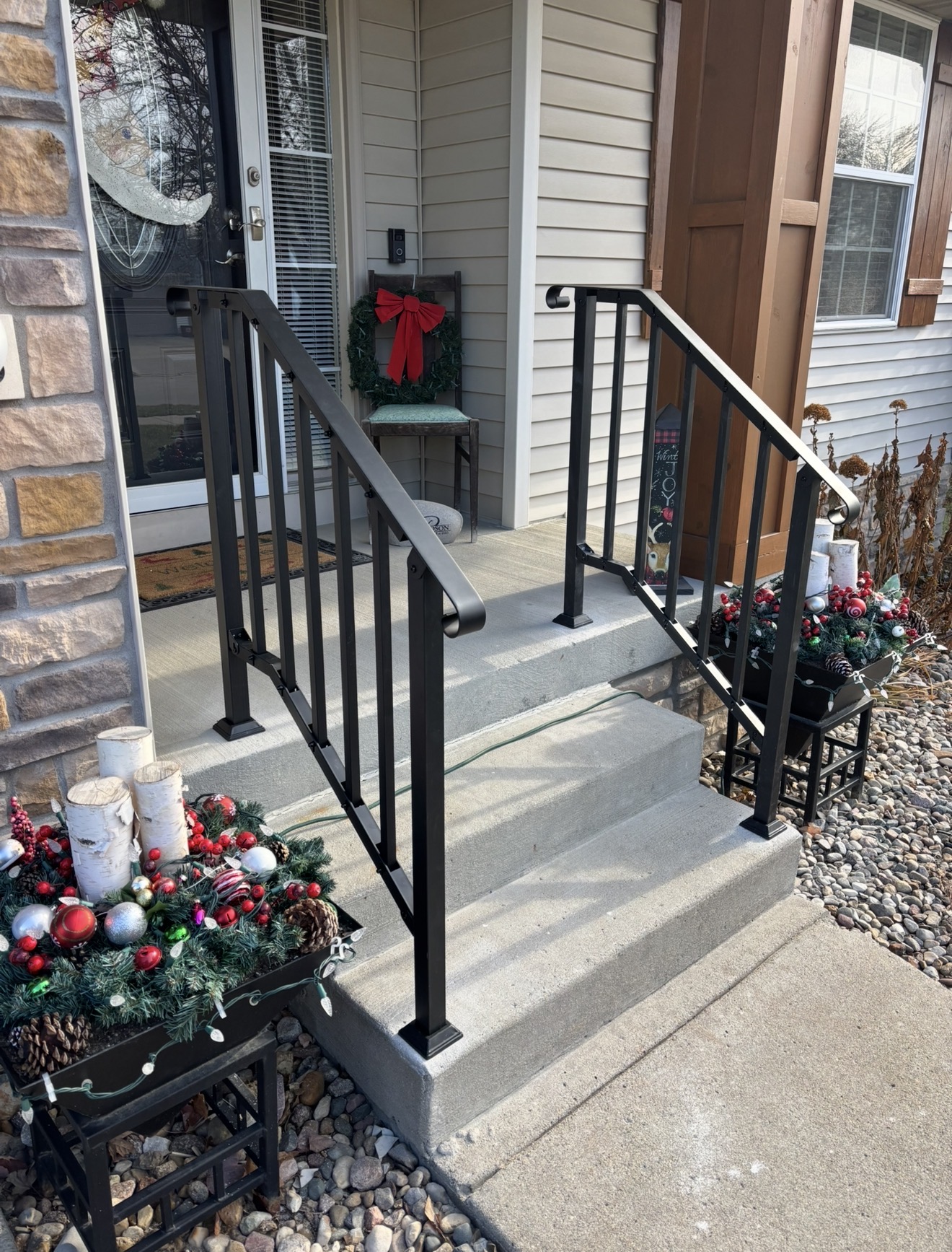 Black metal handrails installed on concrete front steps leading to a home entrance.
