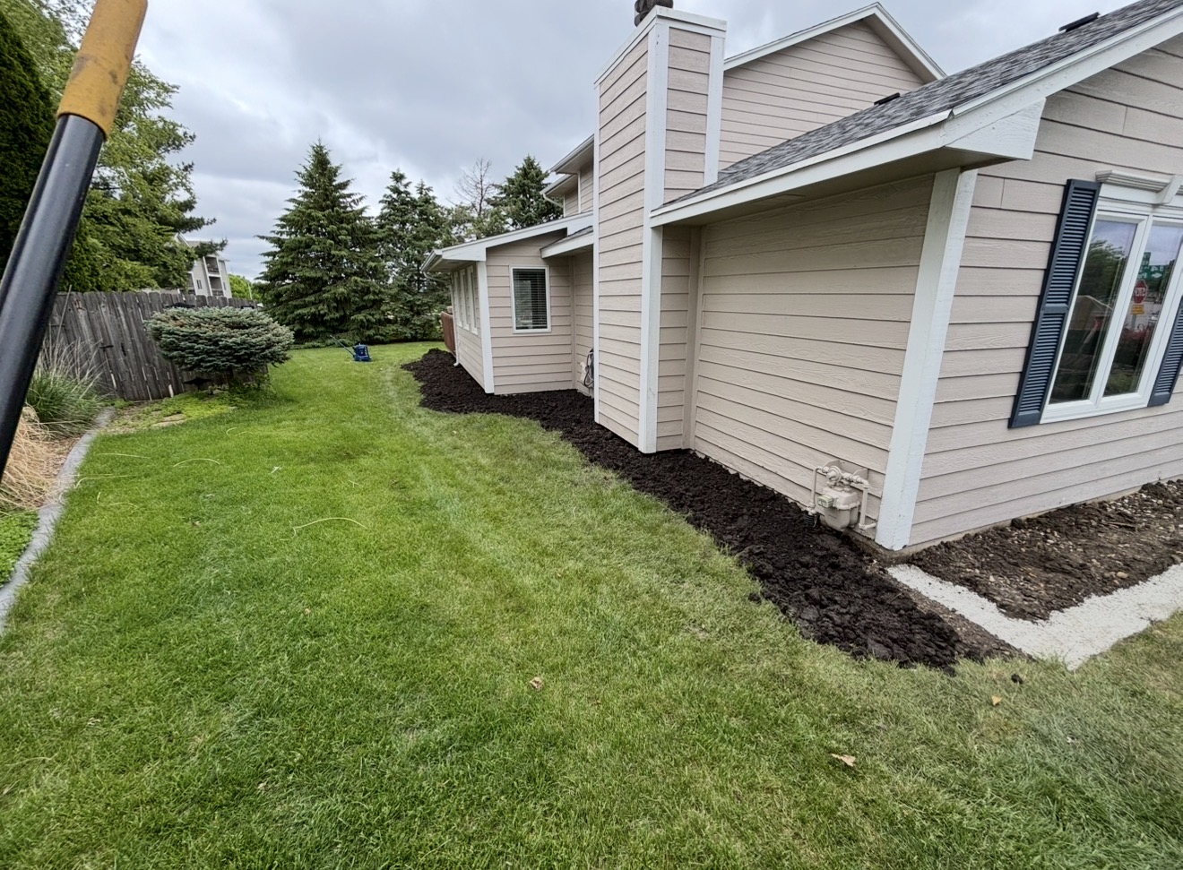Fresh dark soil graded along the foundation of a beige-sided home next to a green lawn.