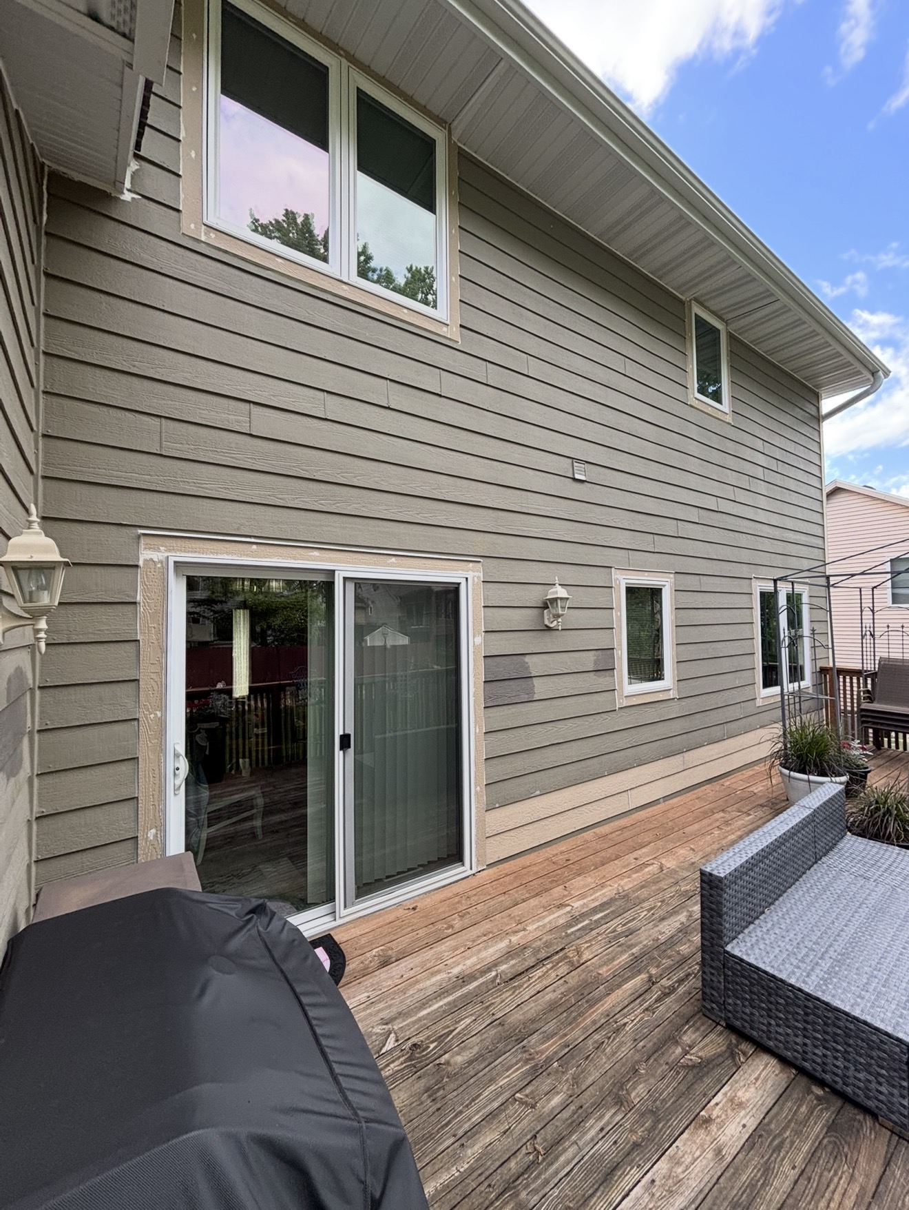 Newly installed white vinyl sliding glass patio door and windows with unfinished wood trim on a house with olive-green siding.
