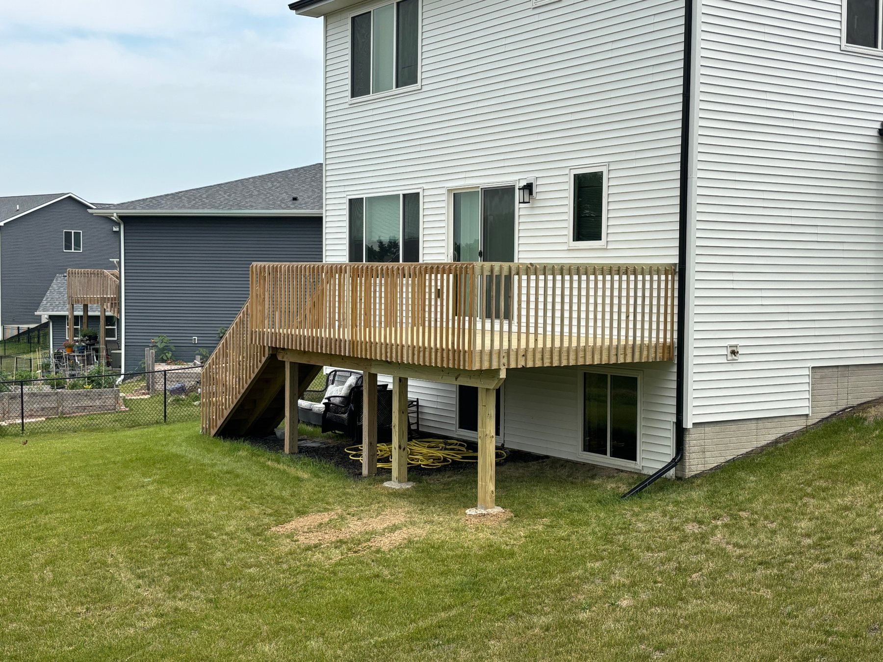An elevated wooden deck with matching wood railings and stairs attached to the back of a white house.